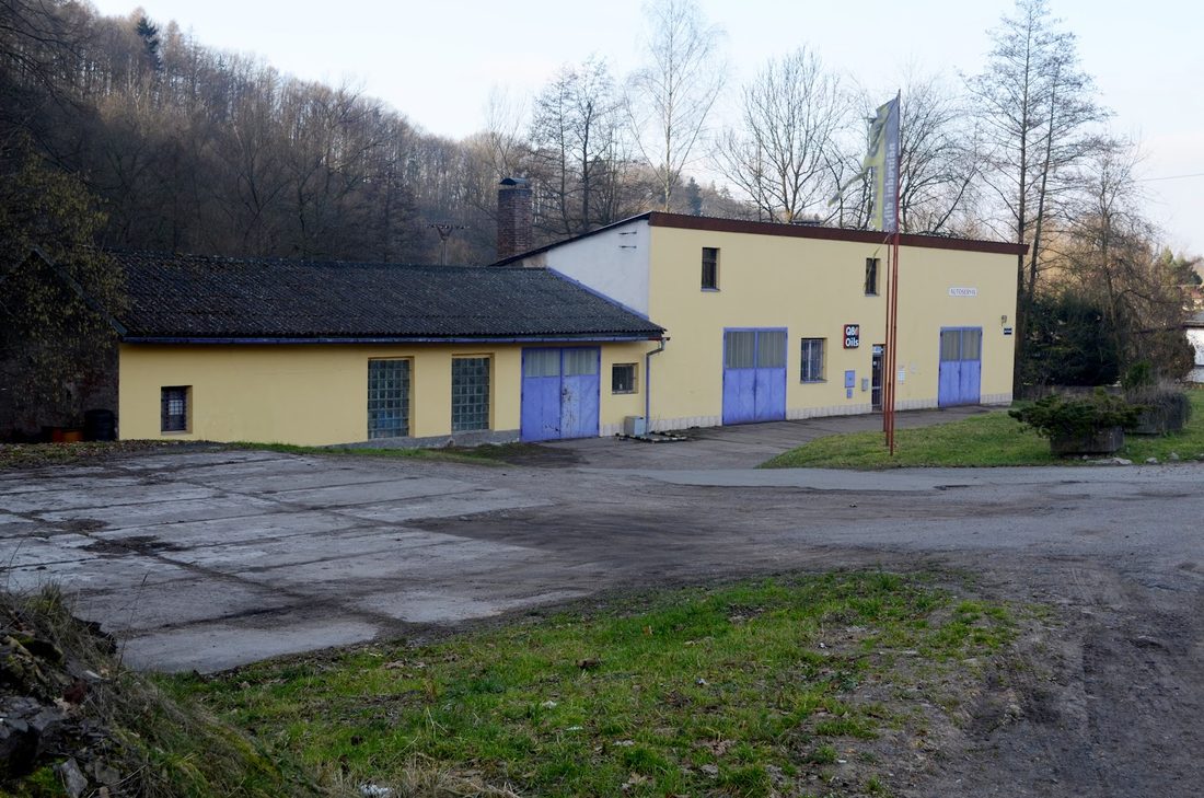 Žlutá budova dílny s modrými vraty a dvůr před ní